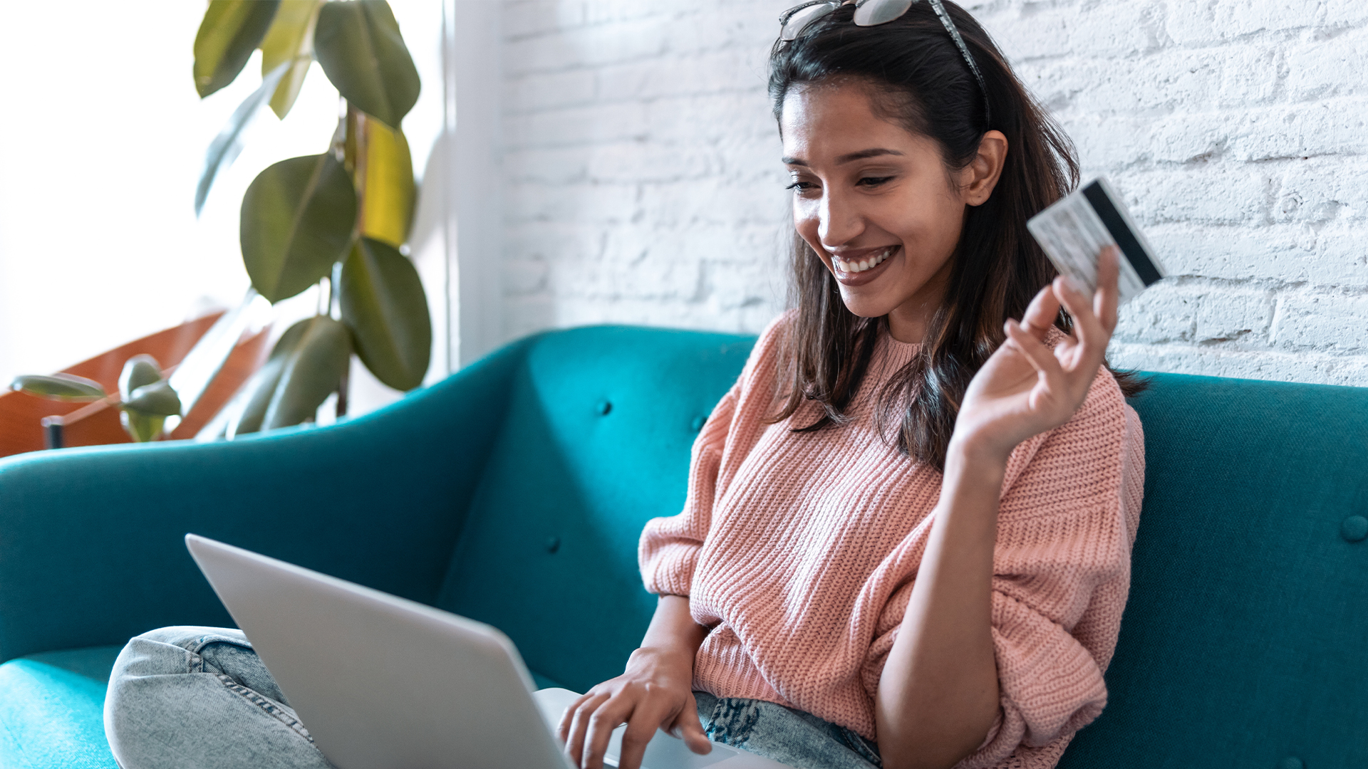 Pretty young woman shopping online with credit card and laptop while sitting on sofa at home.