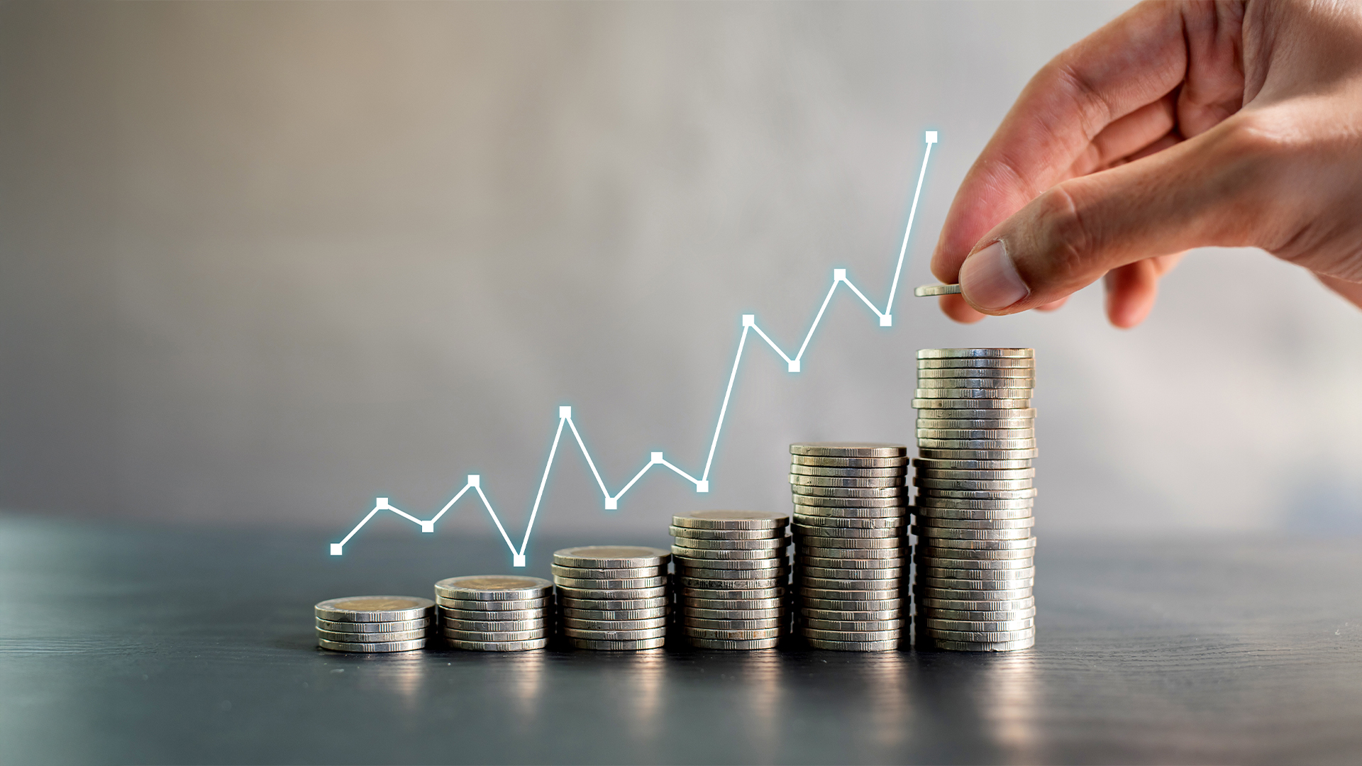 Hand stacking coins on black wooden table with profit line chart growth up.