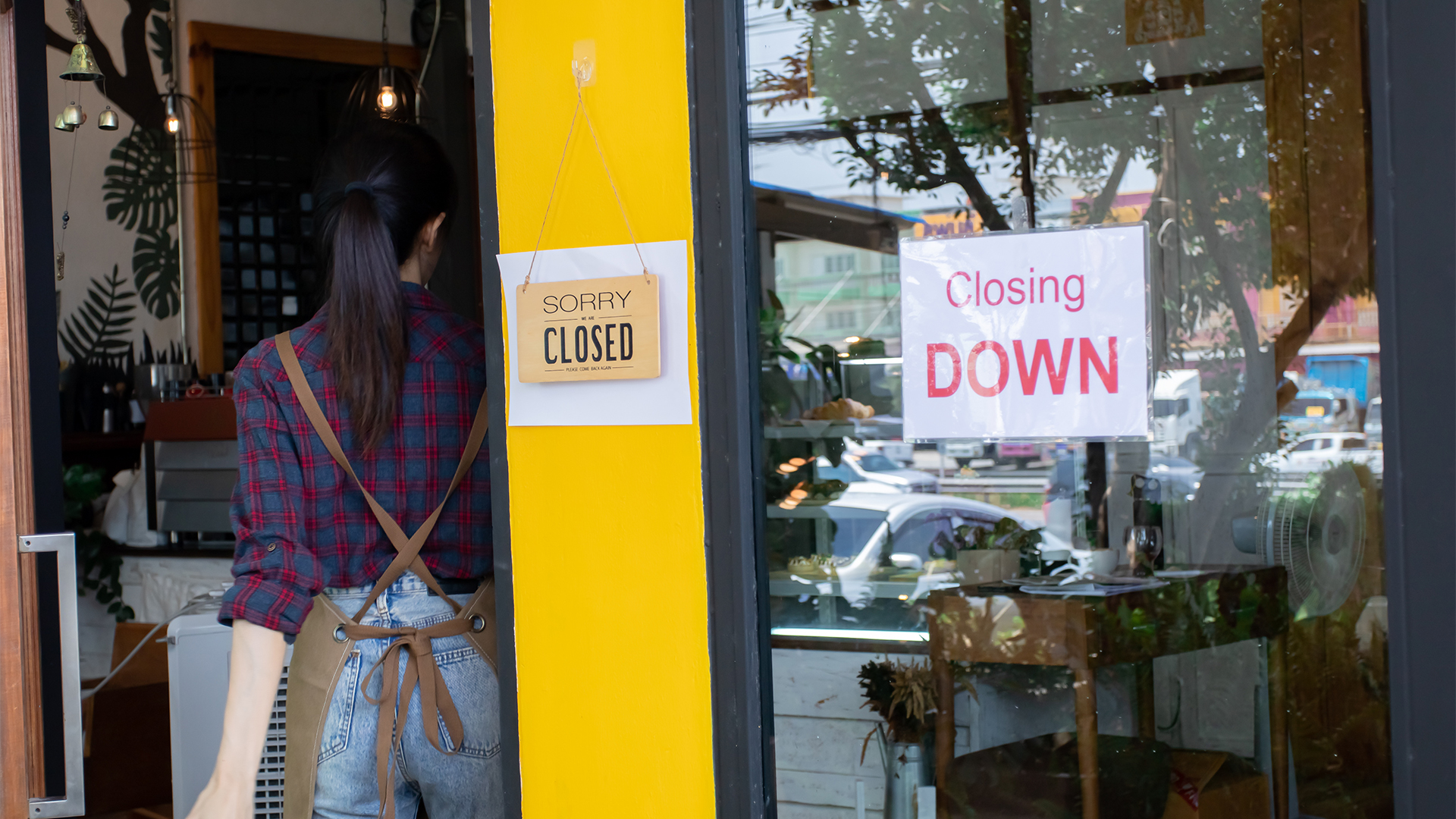 Asian businesswoman stands in front of café looking at a sign closing down, shutting down a small business.
