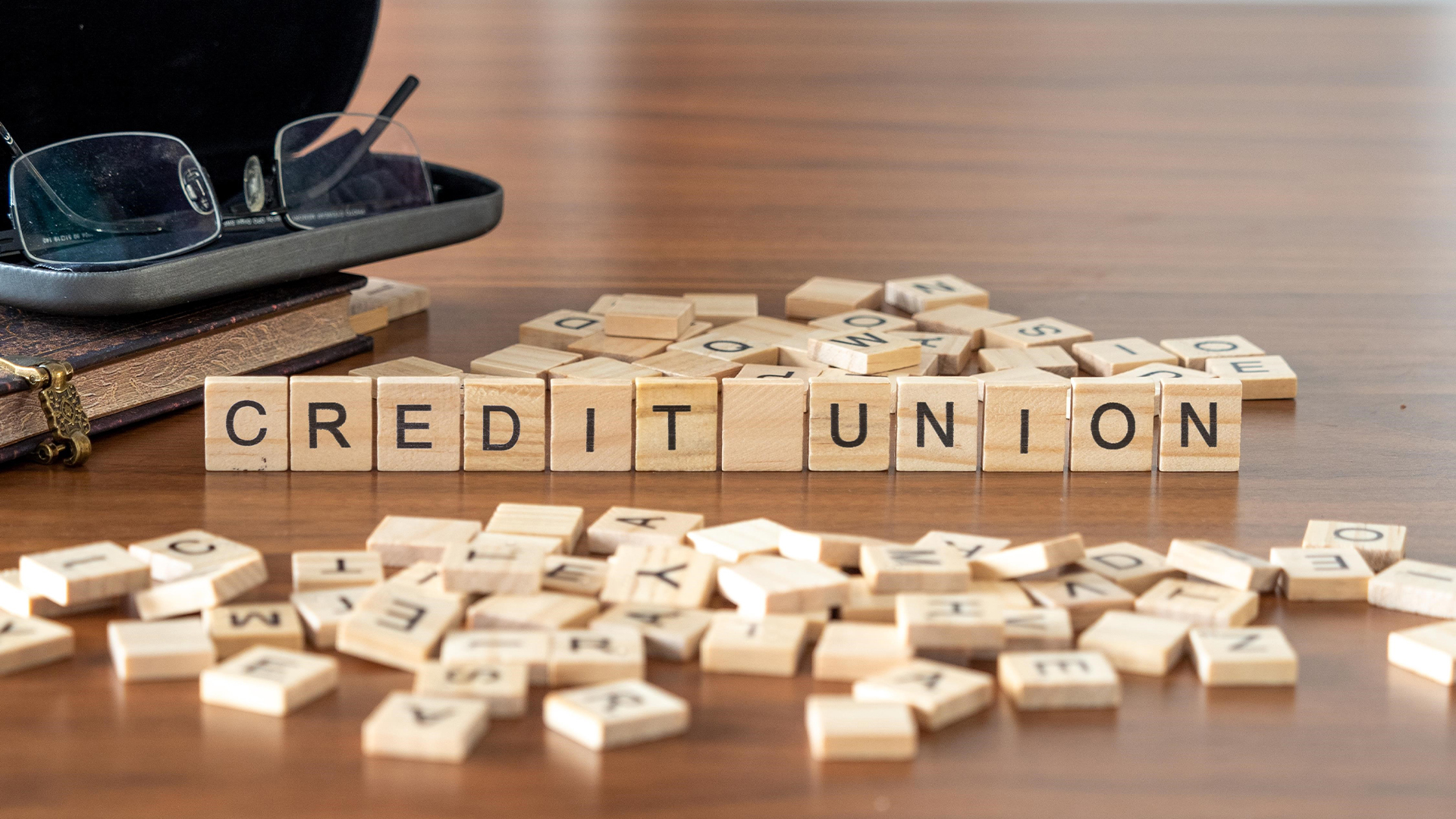 credit union word or concept represented by wooden letter tiles on a wooden table with glasses and a book