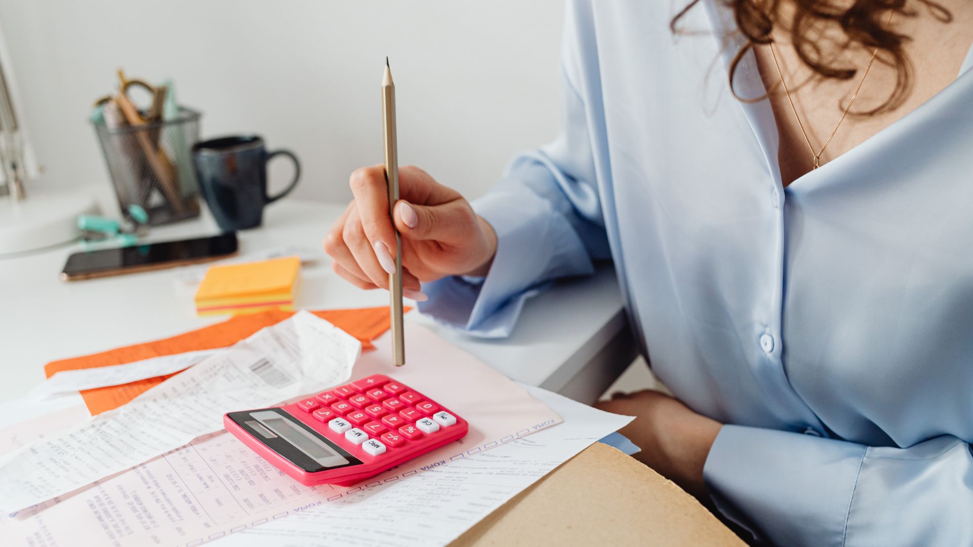 A woman holding a pencil and using a calculator to add up her receipts.