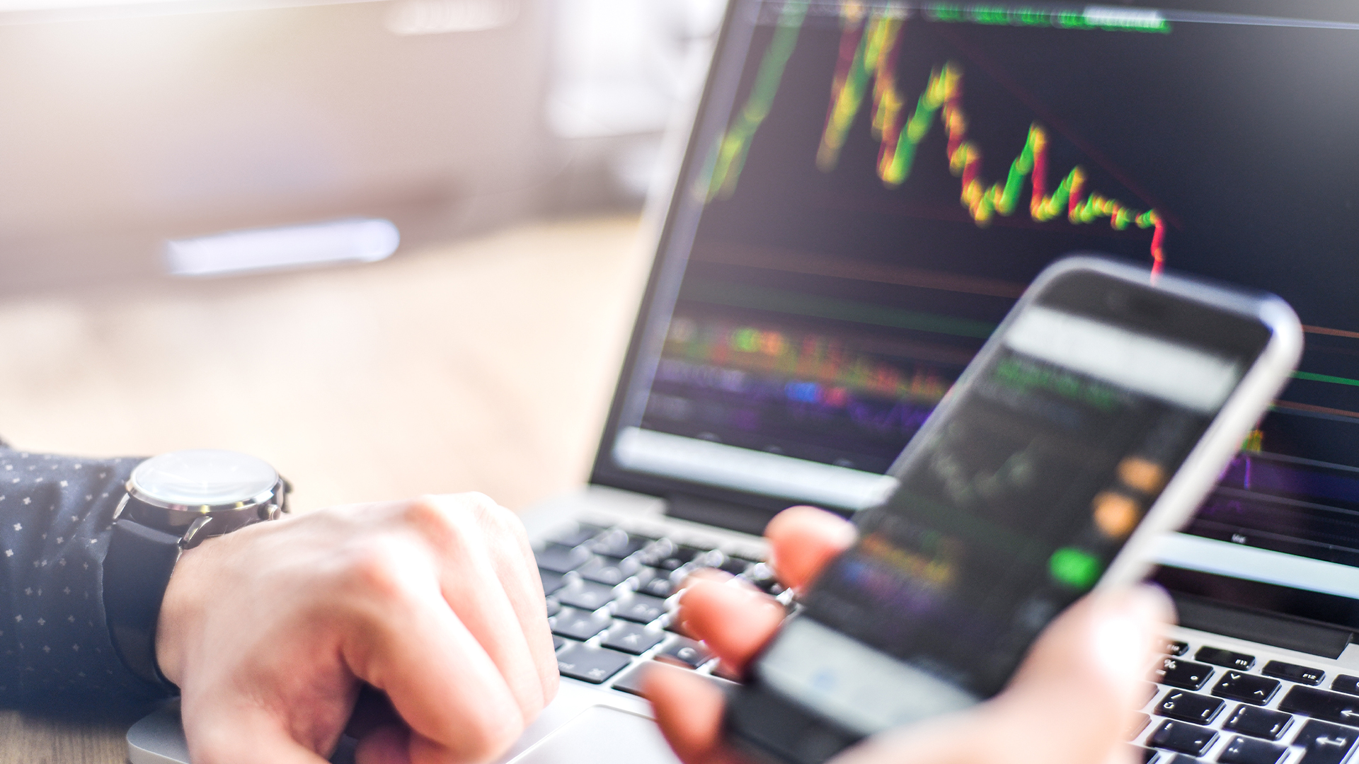 Man holding smartphone in hand and working on laptop, financial bitcoin crypto graph data trade.