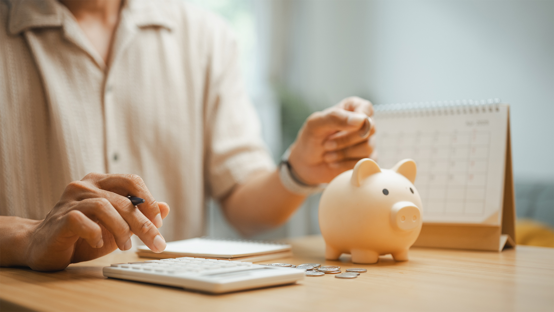 Person managing a budget with a calculator, piggy bank, and monthly planner, representing personal finance